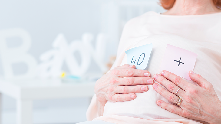 Mulher sentada com a mão na barriga, com um papel colado na roupa escrito: 40 +