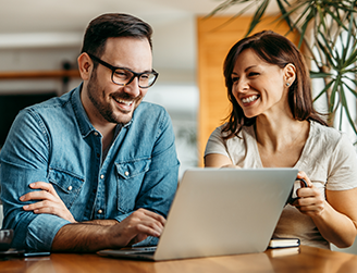 Homem e mulher sorriem enquanto trabalham em um notebook